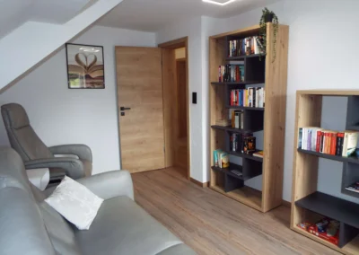 Gemütliches Lesezimmer einer Ferienunterkunft in Bolsdorf (bei Hillesheim) mit grauem Ledersofa, Relaxsessel und Bücherregal.