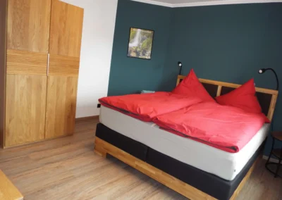 Helles Schlafzimmer einer Ferienunterkunft in Bolsdorf (bei Hillesheim) mit Doppelbett, roter Bettwäsche und dunkelblauer Wand.